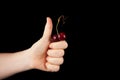 Concept - Food waste reduction. Female hand with thumb up like symbol holds a ripe funny cherry of unusual shape. Ugly cherries