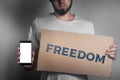 Concept of freedoms and human rights. A man with a cardboard and a phone in his hand. Text freedom and mock up. Dark color Royalty Free Stock Photo