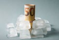 Concept of freezing the funds. Euro money roll inside ice cubes on blue studio background. Royalty Free Stock Photo