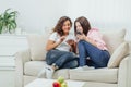 Two roommates using their smartphones at home sitting on a sofa in the living room.