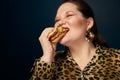 The concept of gluttony. Overweight. Fat woman in a leopard print blouse with a hamburger in her hand.