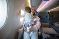 Concept good travel with baby. little cute toddler jumping on her knees with a young beautiful mother in an airplane