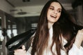 Young cheerful woman drying hair with blowdryer