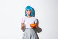 Concept of halloween. Image of attractive skeptical asian girl in blue wig, holding candle and pumpkin, looking serious