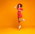 Concept happy emotional young woman in red summer dress and hat jumping on yellow background