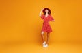 Concept happy emotional young woman in red summer dress and hat jumping on yellow background