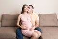 Concept happy family in anticipation of the birth of a baby. Pregnant woman and her husband cuddling on the sofa at home Royalty Free Stock Photo