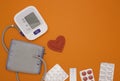 Concept of health, blood pressure, cardiology. Electronic blood pressure monitor, tissue red heart and pills on a bright orange Royalty Free Stock Photo