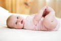 Concept of healthy child. Cute baby lying on her back on bed in room, holding legs with her hands.