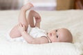 Concept of healthy child. Cute baby lying on her back on bed in room, holding legs with her hands. Royalty Free Stock Photo