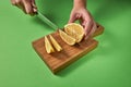 A woman`s hands cutting a half of green ripe lime with slices on a wooden board on a green background. Royalty Free Stock Photo