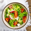 The concept of healthy kitchen. Salad of fresh herbs, radish, cucumber and tomatoes with oil on a white napkin on rustic wooden Royalty Free Stock Photo