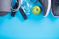 The concept of healthy lifestyle. Sport shoes, bottle of water, apple and yoga mat with copy space on blue background. Exercise eq