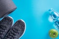 The concept of healthy lifestyle. Sport shoes, bottle of water, apple and yoga mat with copy space on blue background. Exercise eq