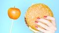 Concept of healthy and unhealthy food. Yaloko against hamburgers on a bright blue background. female hands with red nail