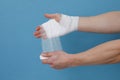 Concept of help during an injury, man wrapping hand in bandage on blue background Royalty Free Stock Photo