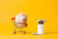 Concept of high cost of medicines. A shopping cart filled with cash and a jar of pills. Yellow background. Copy space Royalty Free Stock Photo