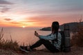 The concept of Hiking and sports recreation. A woman with a backpack on her back sits on a rock and looks at the sunset, holding a Royalty Free Stock Photo