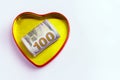 One hundred dollars in a gold heart shaped box with a red outline against a light background. Concept for the holiday St. Valentin Royalty Free Stock Photo