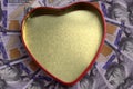 A golden heart box with a red outline against the background of hundred-dollar bills spread out in a circle. Concept for Royalty Free Stock Photo