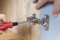 A hand of a furniture assembler adjusting a mechanism for opening the door of the office table with a screwdriver. Close up. Royalty Free Stock Photo