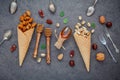 Concept for homemade various nuts ice cream. Mixed nuts in waffle cones ,metal utensils and honey dipper on dark concrete