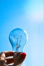 Concept idea of a burning incandescent lamp in a hand against a clear blue sky background from solar energy power Royalty Free Stock Photo