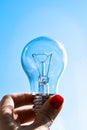 Concept idea of a burning incandescent lamp in a hand against a clear blue sky background from solar energy power Royalty Free Stock Photo