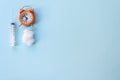 Concept image of waiting for the Covid-19 vaccine. Syringe, cotton ball and ornage alarm clock on a light blue background shot