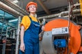 Concept of a industrial manufactory. A female smiling worker in uniform and helmet with a folder in her hand. In the background