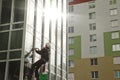 Concept of industry urban works. Industrial mountaineering worker in uniform hangs over residential facade building