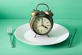 Concept of intermittent fasting, ketogenic diet, weight loss. fork and knife crossed and alarmclock on plate Royalty Free Stock Photo