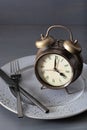 Concept of intermittent fasting, ketogenic diet, weight loss. fork and knife crossed and alarmclock on plate Royalty Free Stock Photo