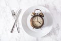 Concept of intermittent fasting, ketogenic diet, weight loss. fork and knife crossed and alarmclock on a plate Royalty Free Stock Photo