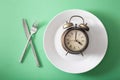 Concept of intermittent fasting, ketogenic diet, weight loss. fork and knife crossed and alarmclock on plate Royalty Free Stock Photo