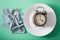 Concept of intermittent fasting, ketogenic diet, weight loss. fork and knife crossed and alarmclock on plate Royalty Free Stock Photo