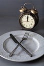 Concept of intermittent fasting, ketogenic diet, weight loss. fork and knife crossed and alarmclock on plate Royalty Free Stock Photo