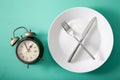 Concept of intermittent fasting, ketogenic diet, weight loss. fork and knife crossed on a plate and alarmclock Royalty Free Stock Photo