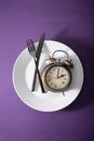 Concept of intermittent fasting, ketogenic diet, weight loss. fork and knife crossed on a plate and alarmclock Royalty Free Stock Photo