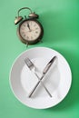 Concept of intermittent fasting, ketogenic diet, weight loss. fork and knife crossed on a plate and alarmclock Royalty Free Stock Photo