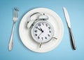 Concept of intermittent fasting, lunchtime, diet and weight loss. Alarm clock on plate Royalty Free Stock Photo