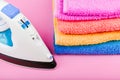 The concept of ironing clothes. House order. Iron and ironed fabric. Electric iron on a pink background with towels. multi-colored Royalty Free Stock Photo