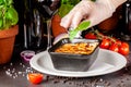 The concept of Italian cuisine. Baked lasagna in a black ceramic baking dish. The chef decorates the dish in the restaurant