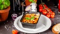 The concept of Italian cuisine. Baked lasagna in a black ceramic baking dish. The chef decorates the dish in the restaurant