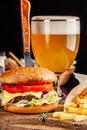 The concept of Italian cuisine. Italian burger with french fries on a wooden board and a glass of light beer with foam