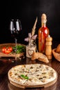 The concept of Italian cuisine. Thin cheese pizza with mushrooms, with large sides of Semola flour. A string of red wine