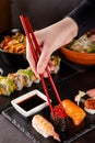 The concept of Japanese cuisine. A girl holds a red Chinese chopsticks and eat sushi in a restaurant. background image Royalty Free Stock Photo