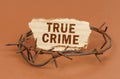 On a brown surface, barbed wire and a cardboard sign with the inscription - True Crime