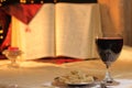 Concept Lord`s Supper and Christian communion. Bread and wine in chalice are front of big Bible. Cross reflect in goblet, candle Royalty Free Stock Photo