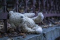 Concept: Lost childhood and loneliness. Dirty teddy bear lying down outdoors. Copy space. Horizontal image